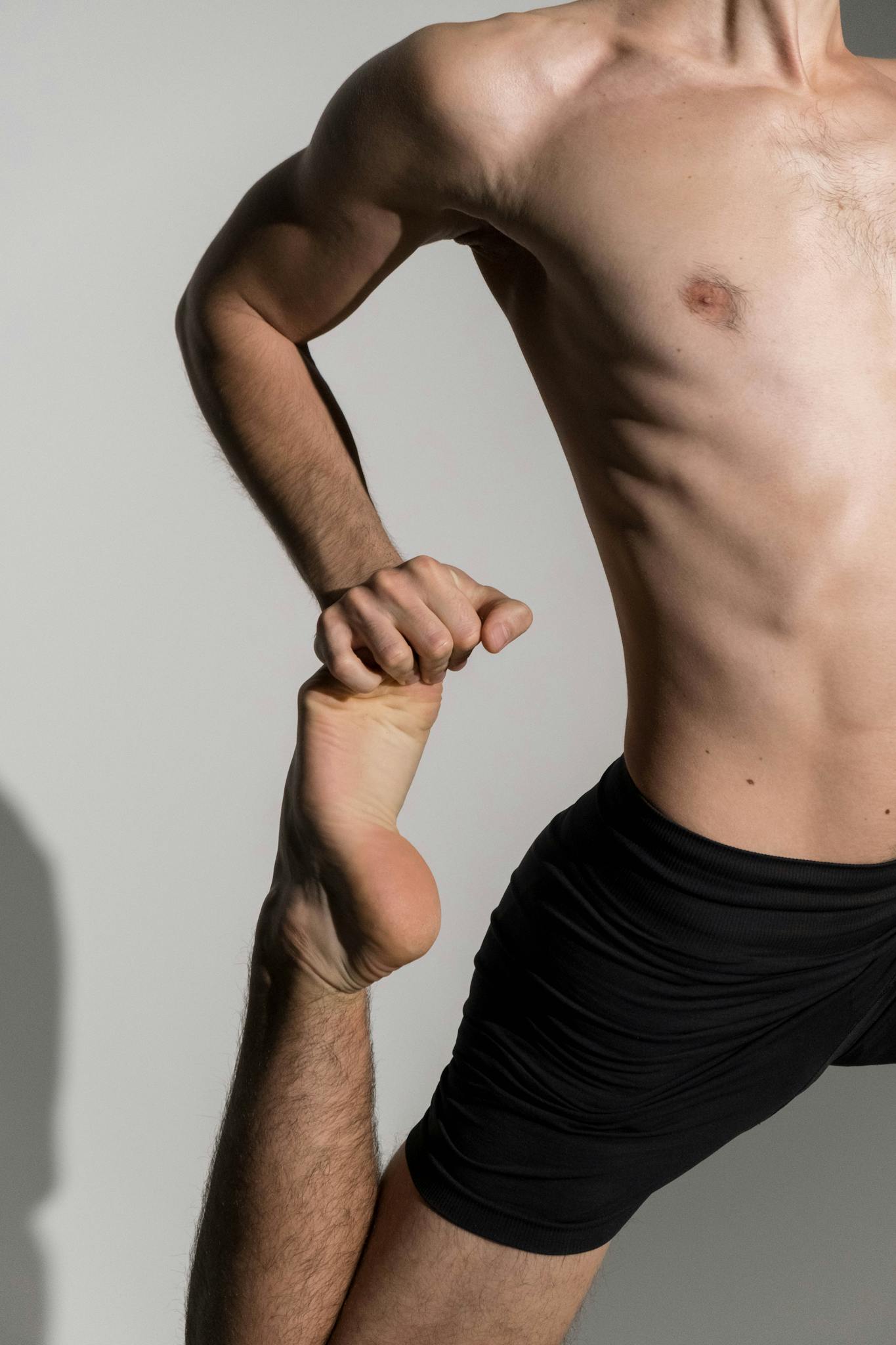 A muscular man performs a standing leg stretch, showcasing flexibility and fitness.