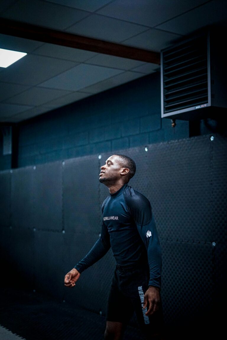 African American athlete in training gear standing indoors against a black wall.